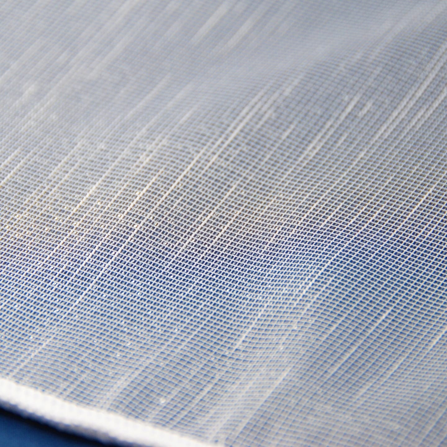Biały materiał z drobnym wzorem siatki, tekstura tkaniny w zbliżeniu, idealna na zasłony lub moskitiery.