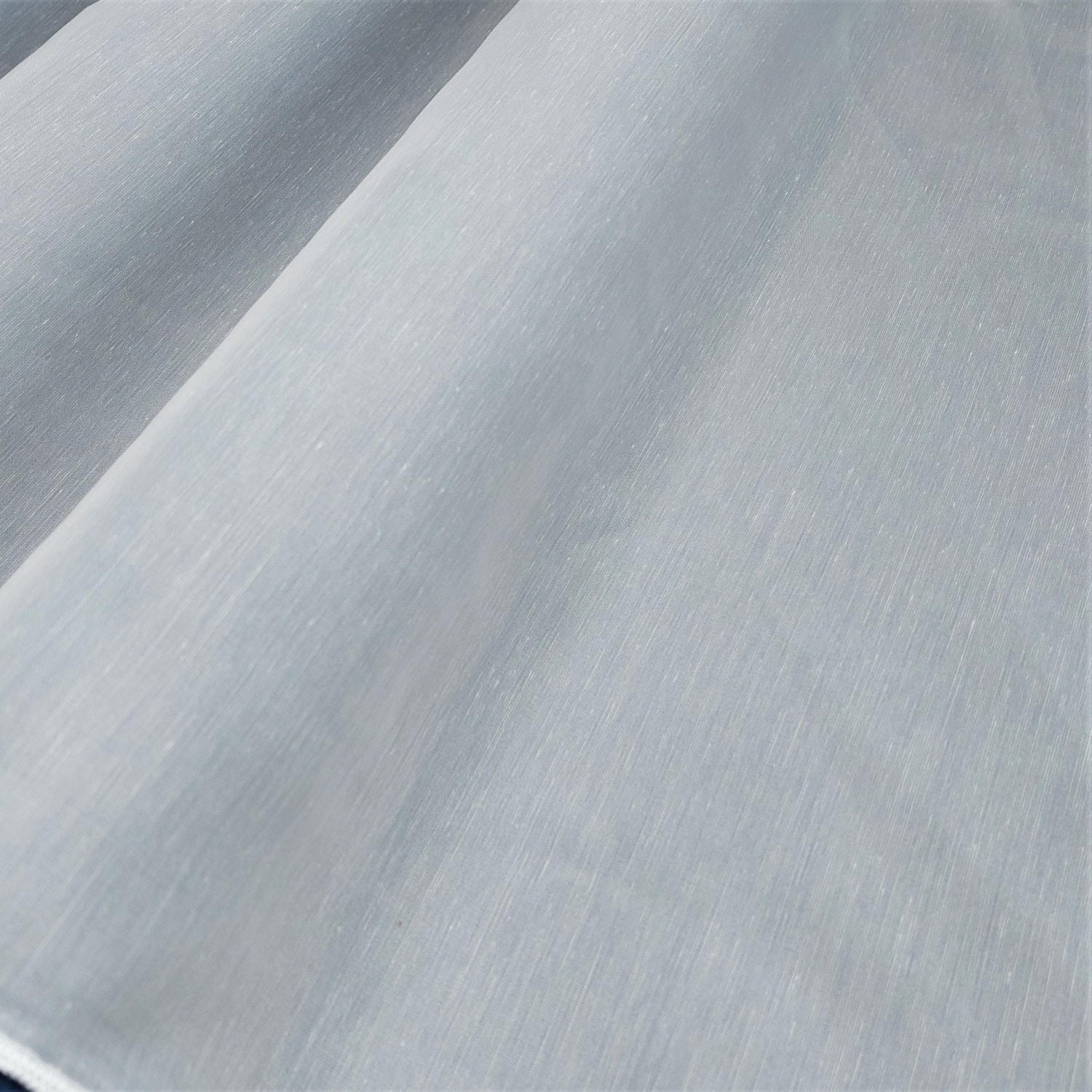 Gładka, szara tkanina poliestrowa ukazana z bliska, pod kątem, pokazująca strukturę materiału.