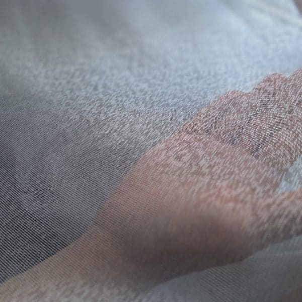 Dłoń dotykająca delikatnej, przezroczystej tkaniny w zbliżeniu.