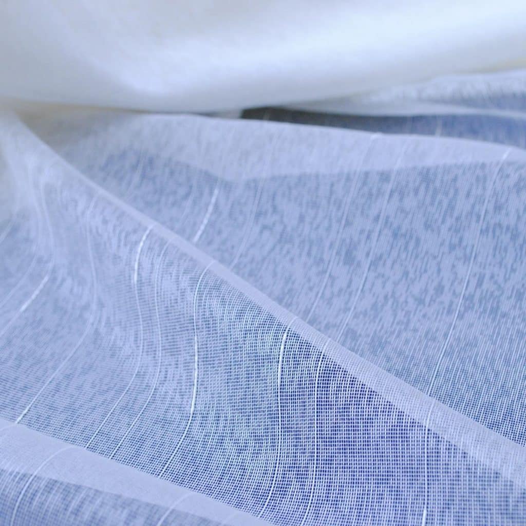 Przezroczysta tkanina w białym kolorze z delikatnym wzorem, układająca się w miękkie fale.