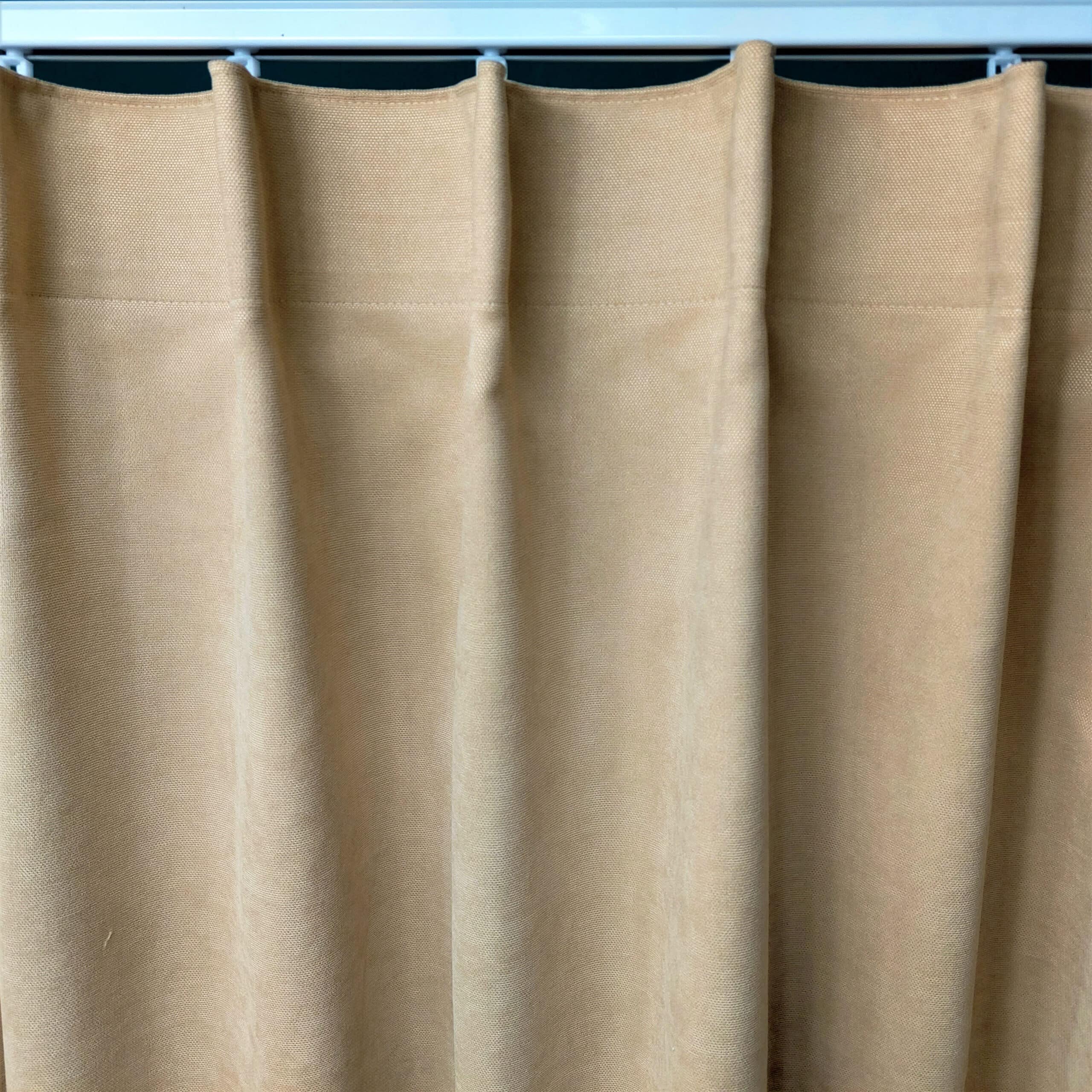 Beżowa zasłona z tkaniny, zawieszona na metalowym karniszu, w klasycznym stylu plisowania.