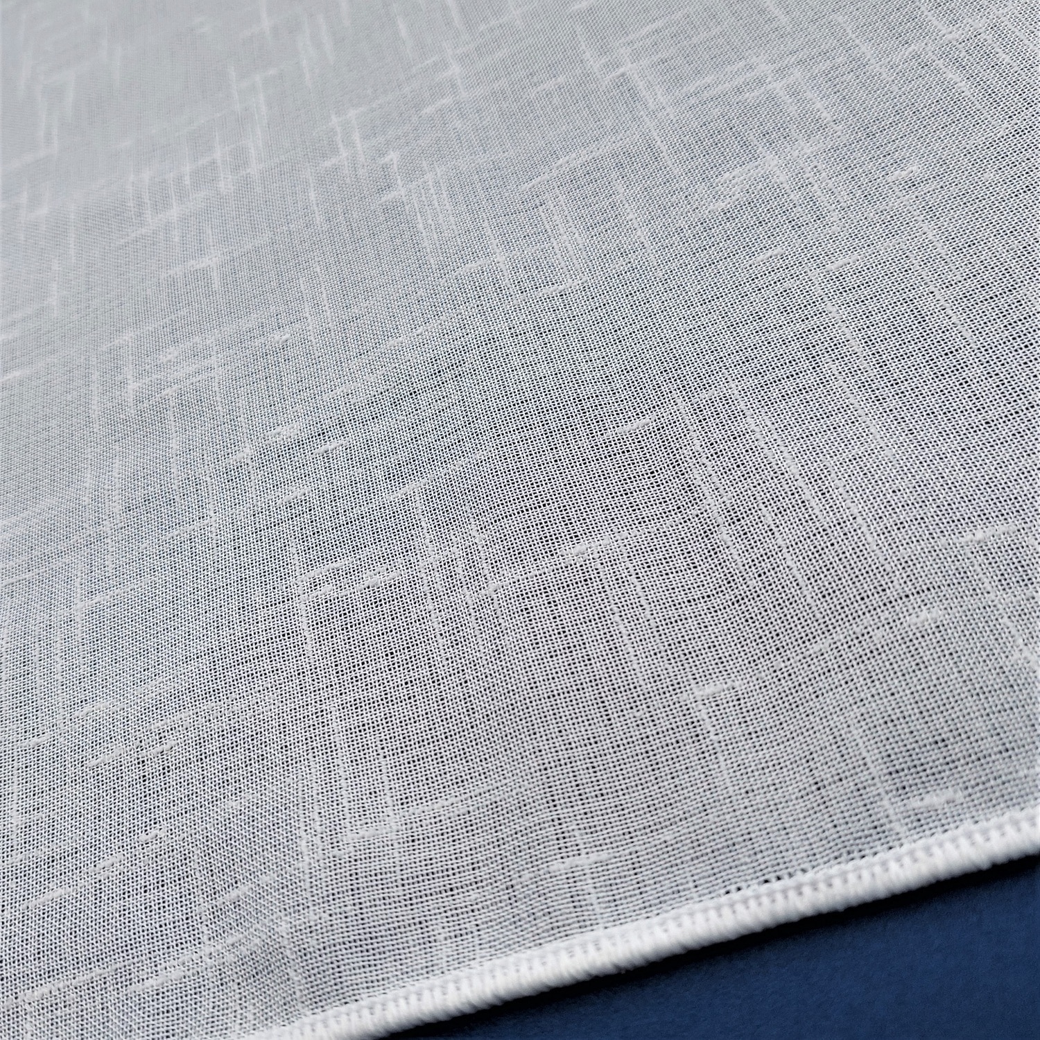 Biała tkanina o fakturze siatki na granatowym tle, zbliżenie na detale materiału.
