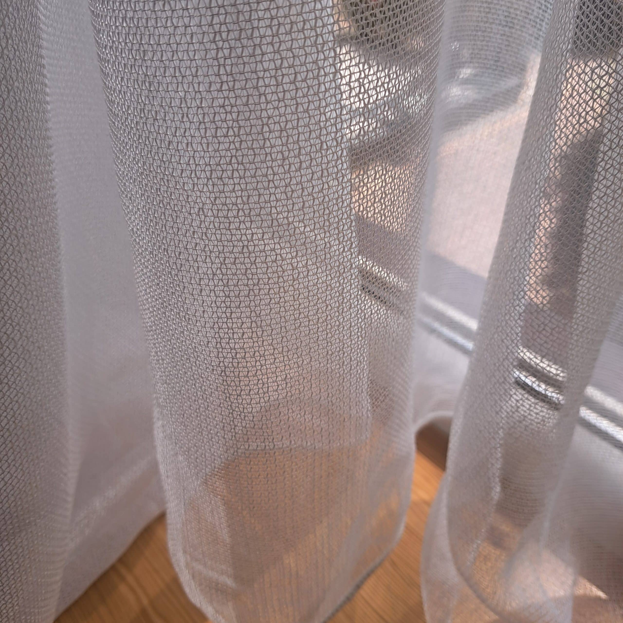 302 bi 1 Prześwitująca zasłona z siateczkowego materiału, przez którą widać promienie słońca padające na podłogę.