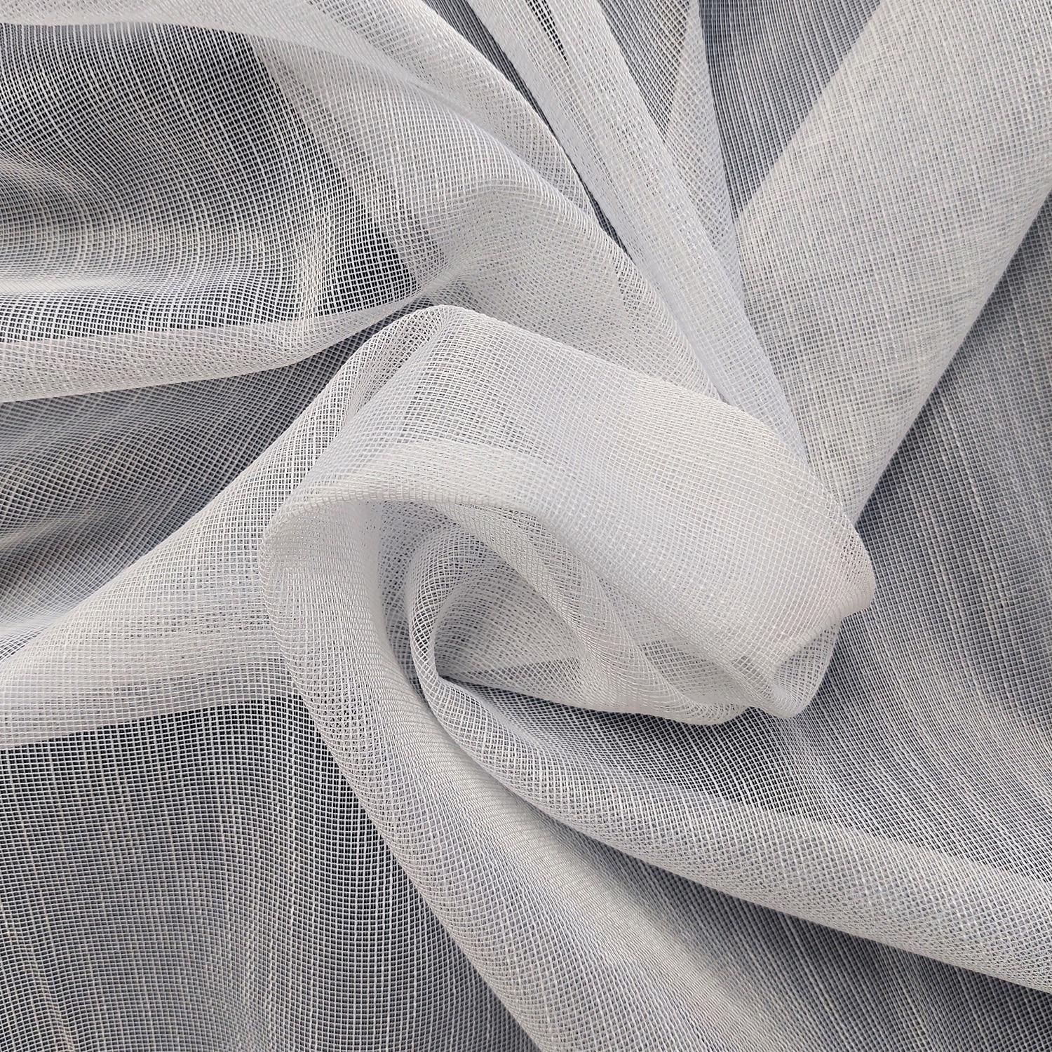 Biały materiał siatkowy złożony w artystyczne fałdy, tkanina o drobnej strukturze idealna do dekoracji i krawiectwa.
