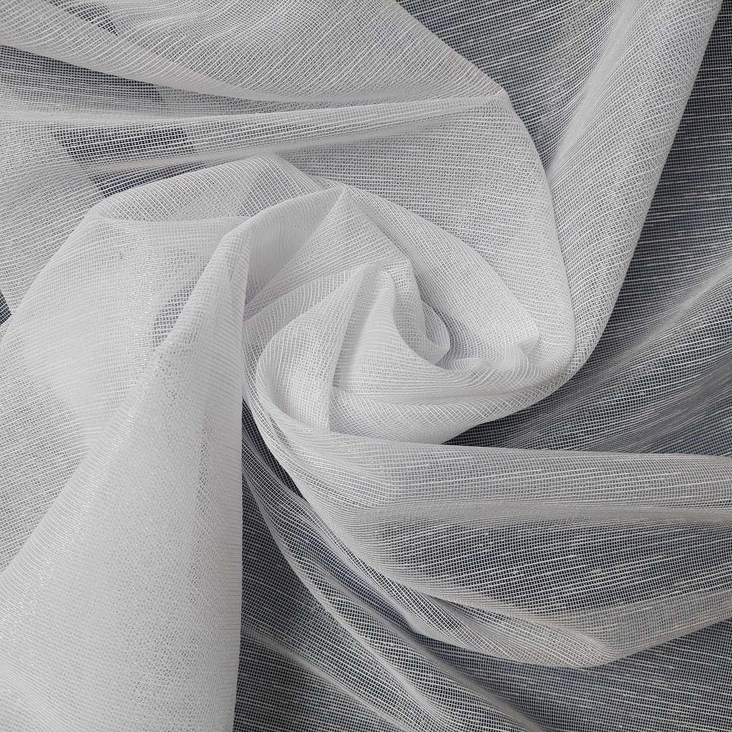 Biała tkanina o delikatnym splocie ułożona w artystyczne fałdy, tworząca elegancki wzór na ciemnym tle.