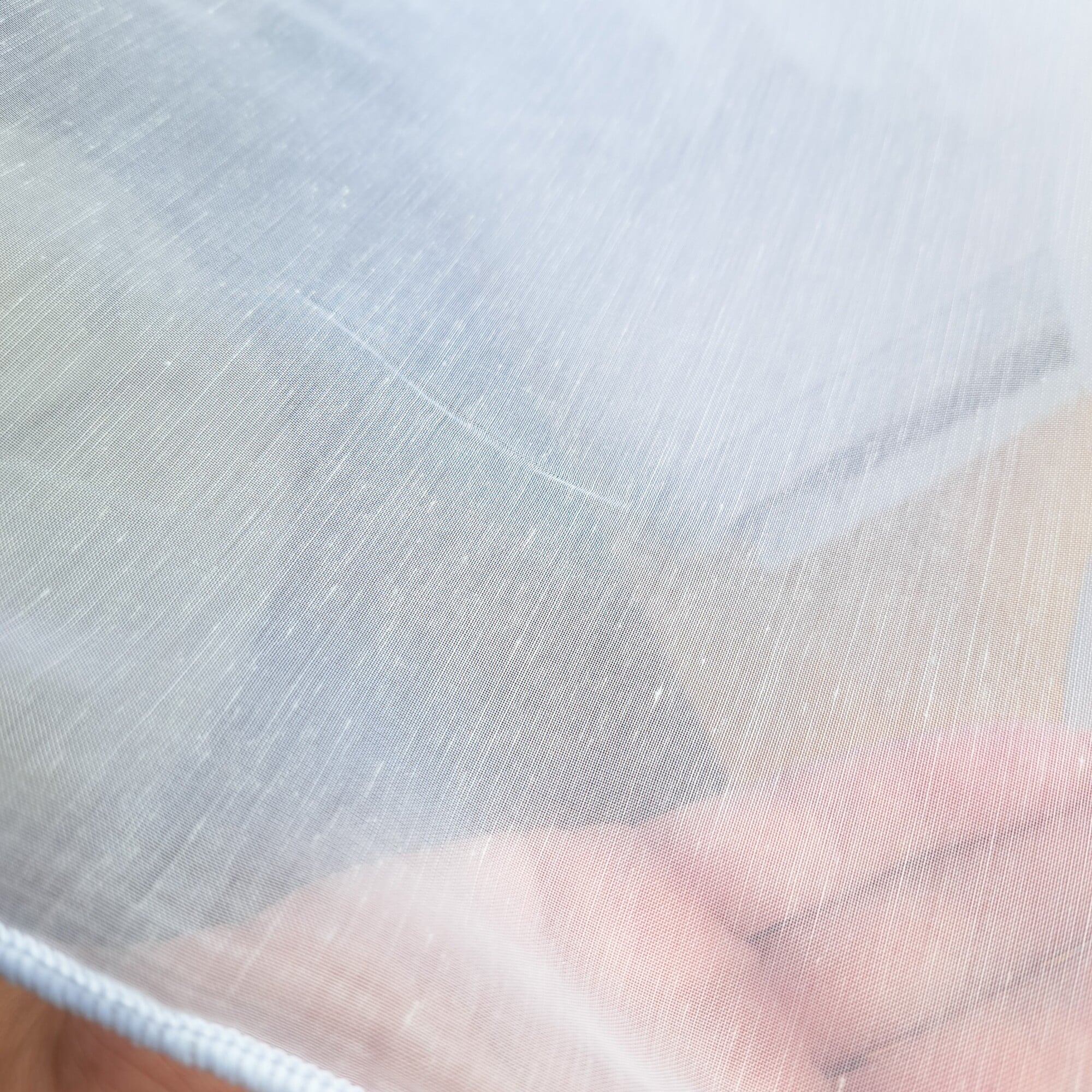 Dłoń dotykająca przezroczystą tkaninę lub siatkę, ukazująca teksturę materiału na tle rozmytych kolorów.