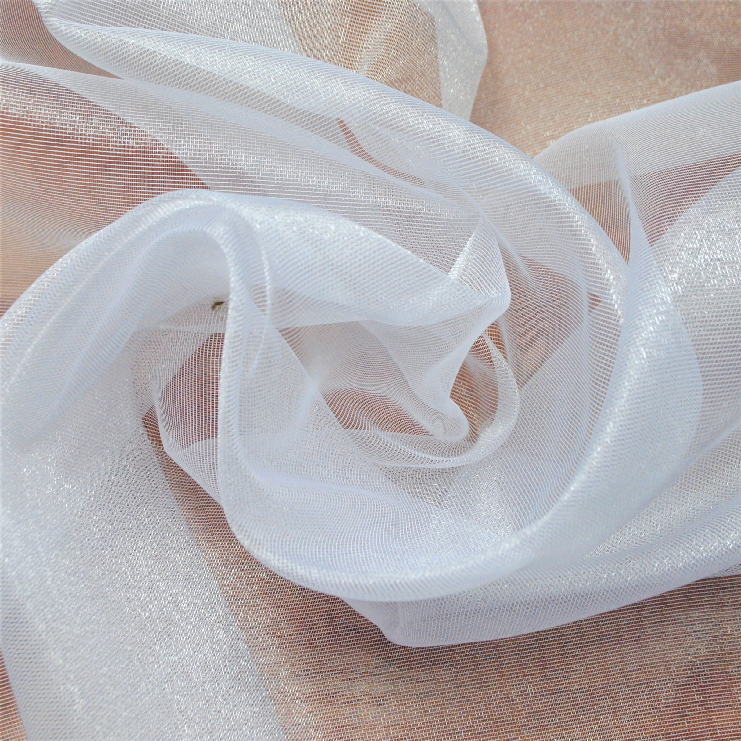 Przezroczysta, zwiewna biała tkanina na tle beżowym, miękko ułożona we wzory.