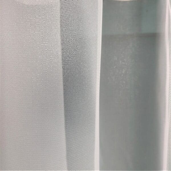 Biała zasłona z delikatnej siatki zawieszona w oknie, przepuszczająca światło dzienne.