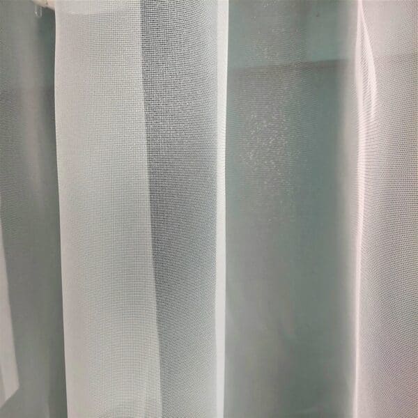 Biała, przezroczysta zasłona wnętrzowa z delikatnym wzorem. Idealna do dekoracji okien domowych.