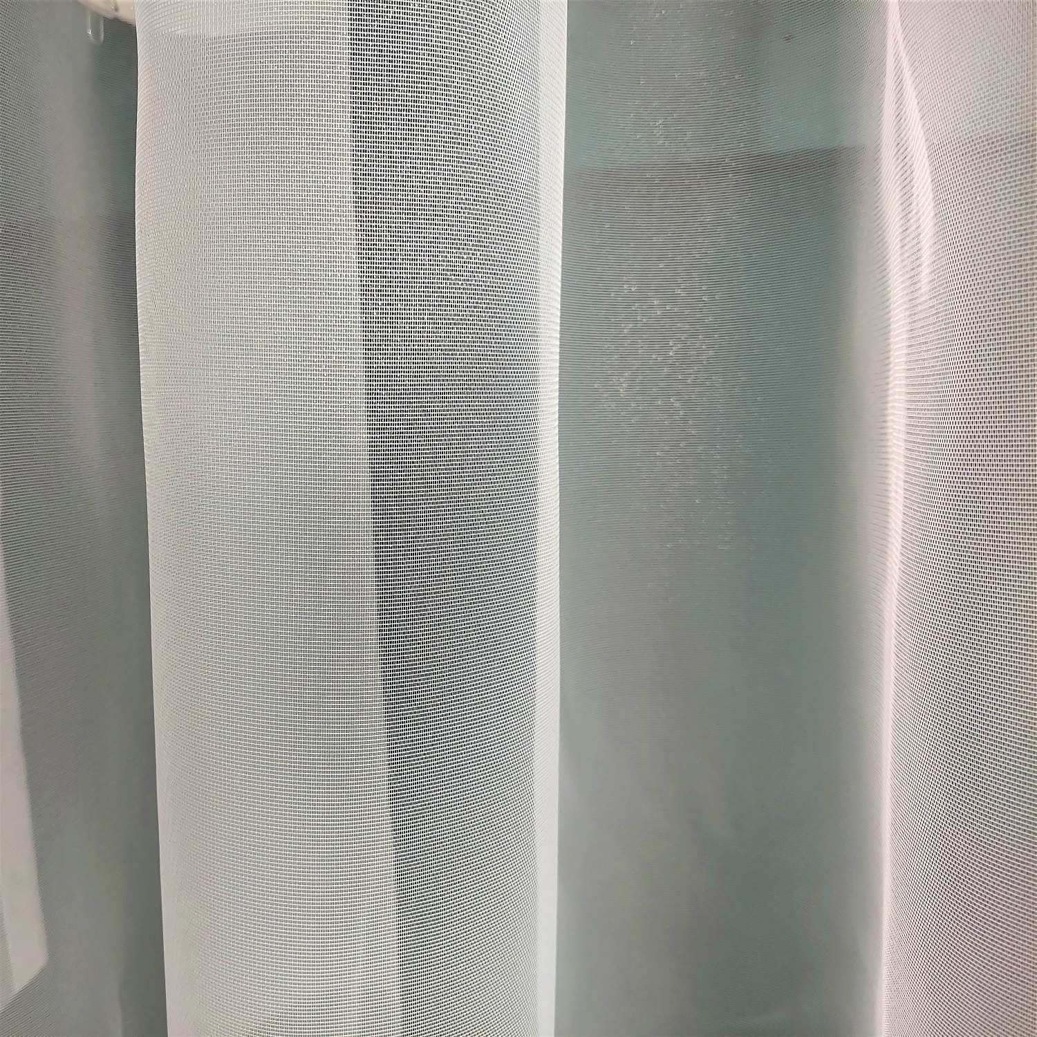 Biała, przezroczysta zasłona wnętrzowa z delikatnym wzorem. Idealna do dekoracji okien domowych.