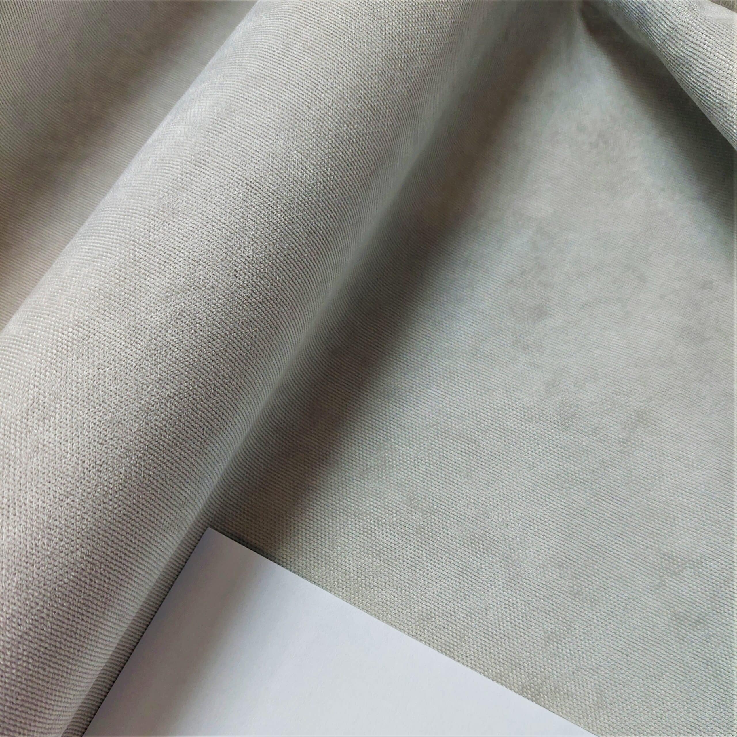 Szara tkanina z delikatną fakturą, ułożona w fałdy obok białej kartki papieru.