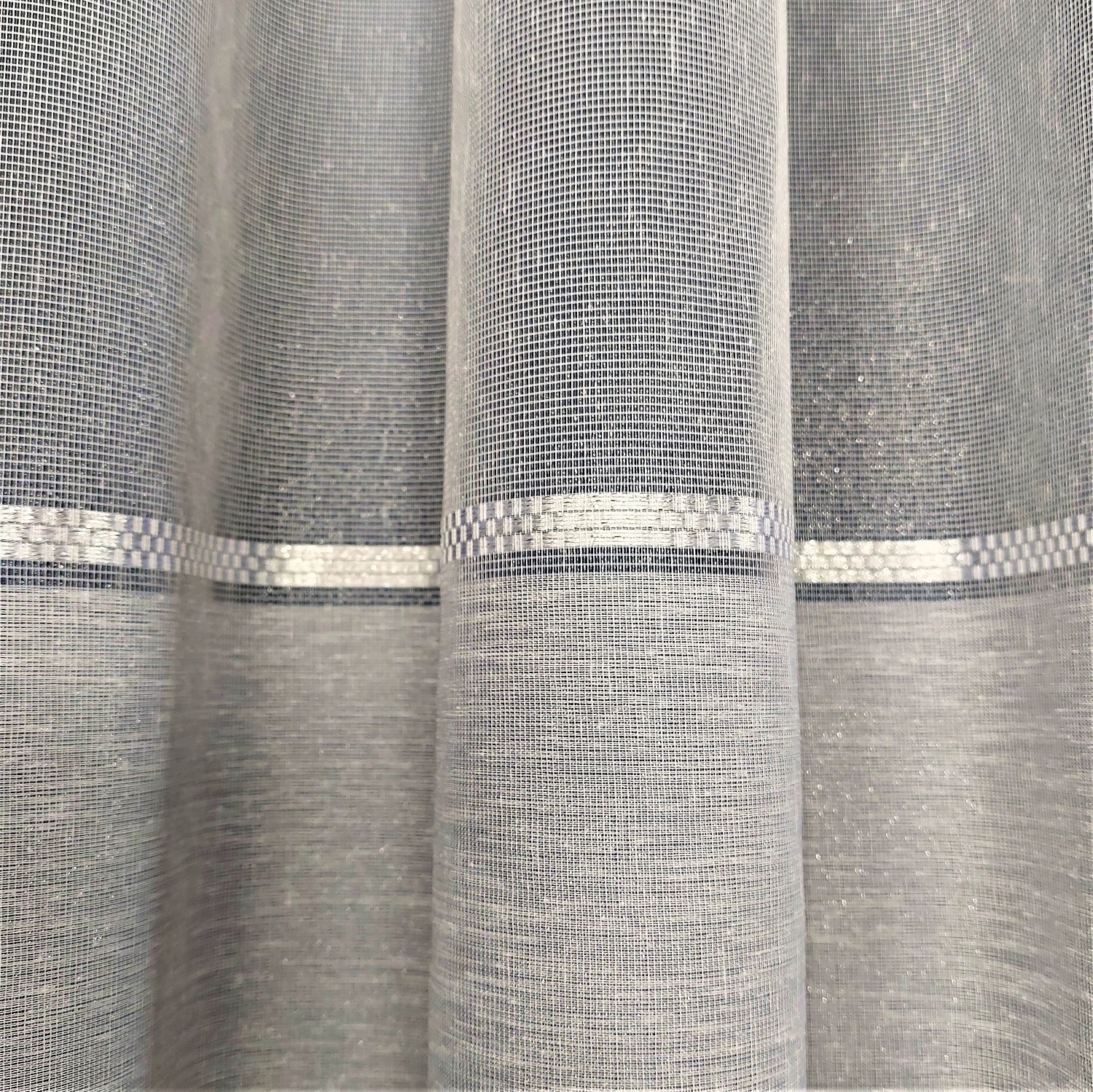 Szare zasłony z delikatnym wzorem, elegancko układające się w pionowe fałdy. Idealne do nowoczesnych wnętrz.