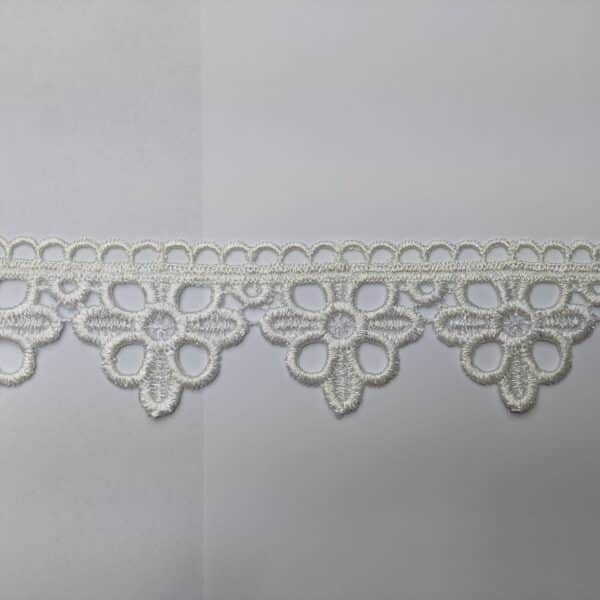 Biały koronkowy wzór na tle, delikatne zdobienia w kształcie kwiatów.