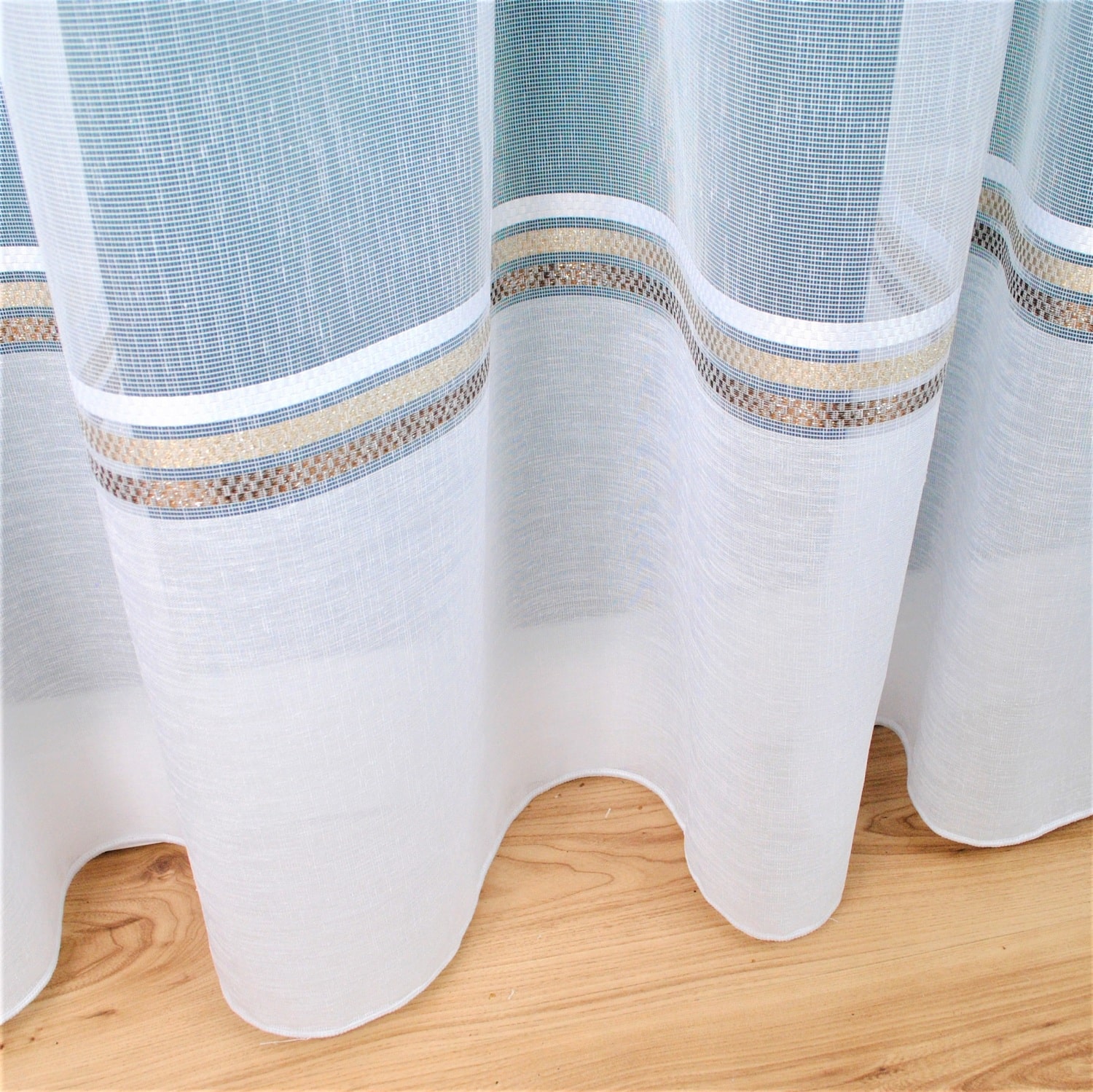 Biały tiulowy firan z kolorowym wzorem, wiszący na drewnianej podłodze. Elegancka dekoracja wnętrza.