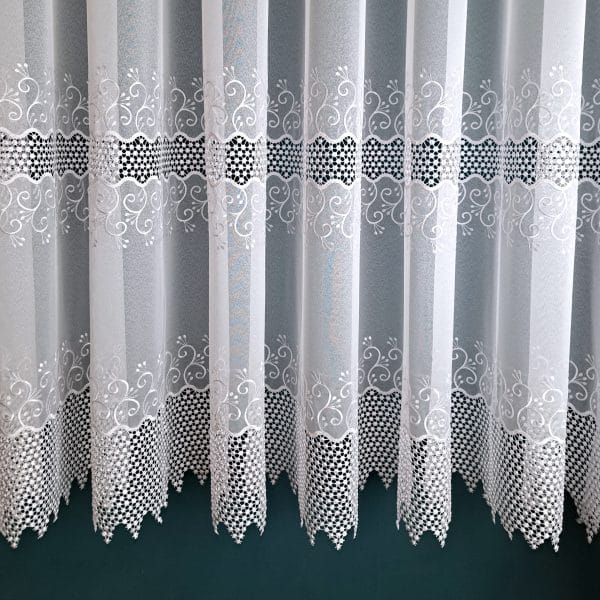 Firany z delikatnym, białym haftem na szarym tle, ozdobione wzorami kwiatowymi i kratką.