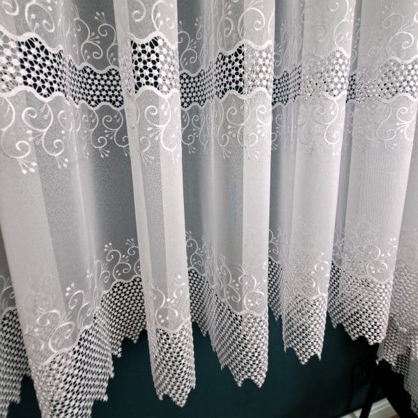 Białe firanki z delikatnym wzorem i ażurowym wykończeniem, elegancka dekoracja okienna.