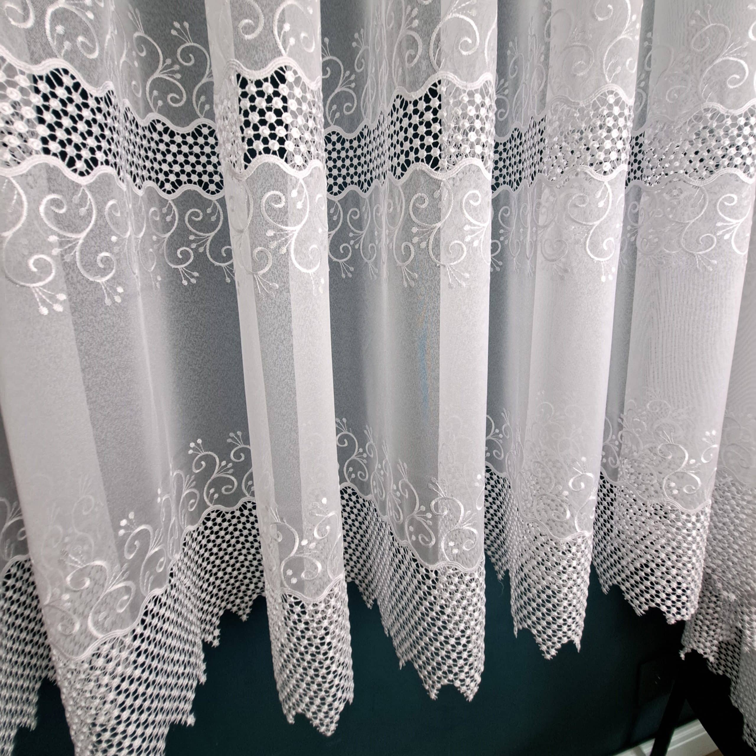 Białe firanki z delikatnym wzorem i ażurowym wykończeniem, elegancka dekoracja okienna.