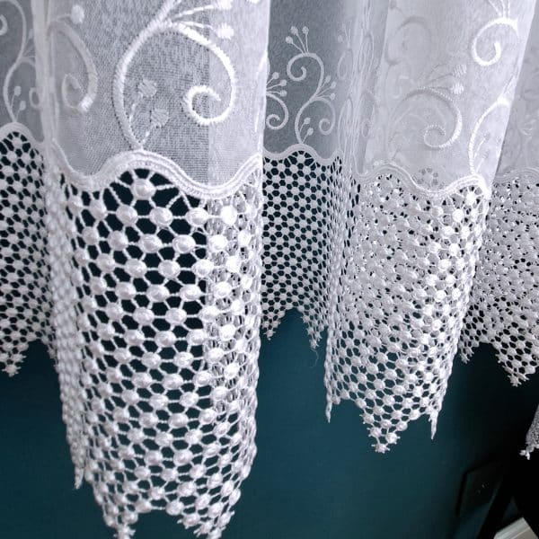 Koronkowa firanka z delikatnym wzorem na tle ciemnej ściany, elegancka dekoracja wnętrza.