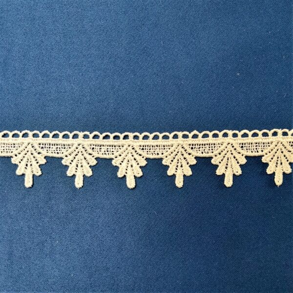 Koronkowa tasiemka z delikatnym wzorem, ułożona na niebieskim tle.