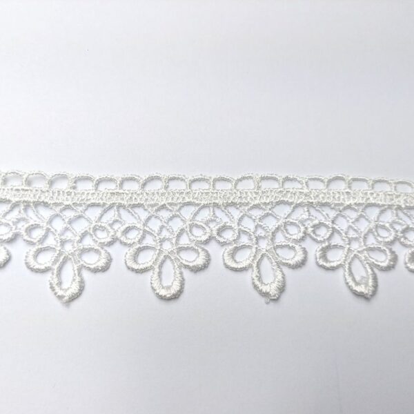 Koronka w kolorze białym na tle białej powierzchni, skomplikowany wzór kwiatowy.