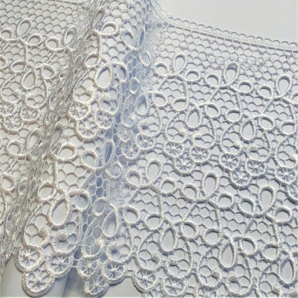 Biała koronka o delikatnym, ażurowym wzorze na tle neutralnym. Idealna do dekoracji i szycia odzieży.