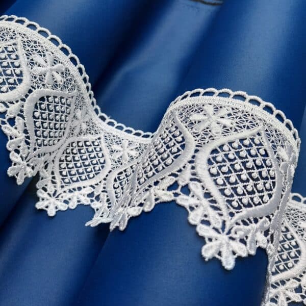 Błękitna satyna z białą koronką o delikatnym wzorze floralnym, układana w fałdy.