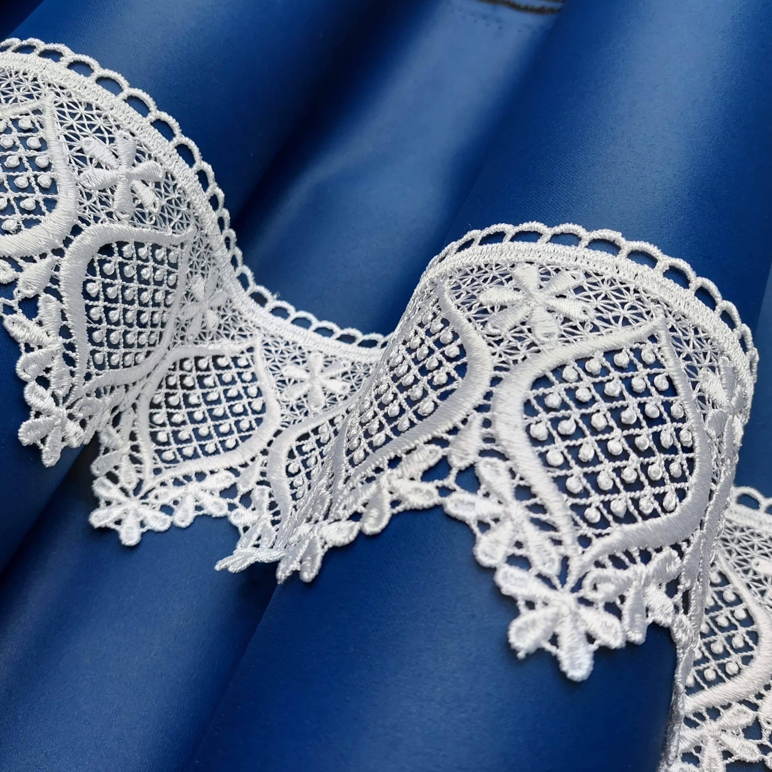 Błękitna satyna z białą koronką o delikatnym wzorze floralnym, układana w fałdy.