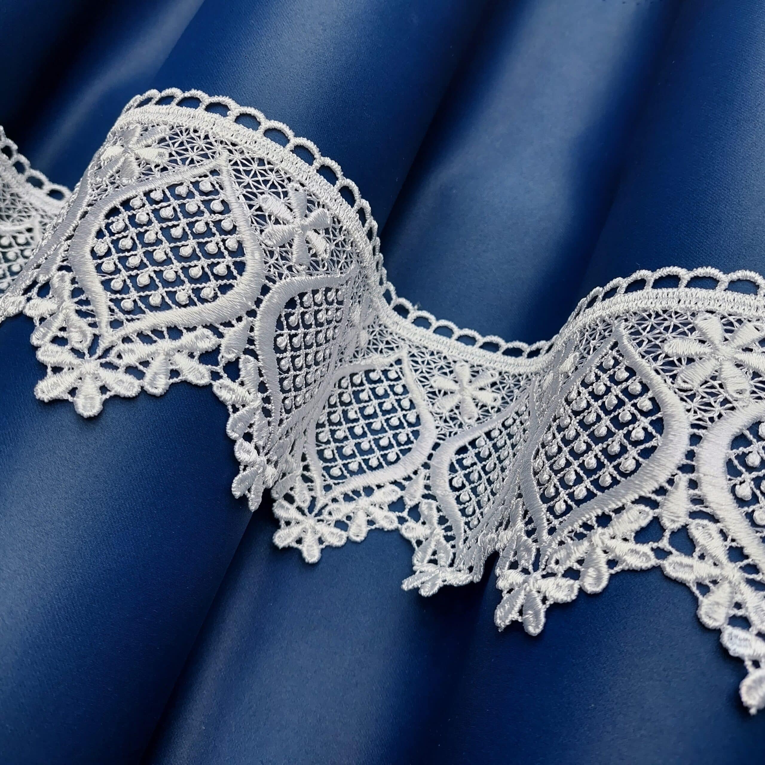 Koronkowa biała tkanina na tle niebieskiego materiału, elegancki wzór tekstyliów.