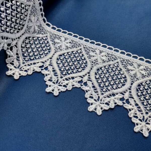 Biała koronka z detalem geometrycznym na niebieskim tle, elegancki wzór ozdobny.