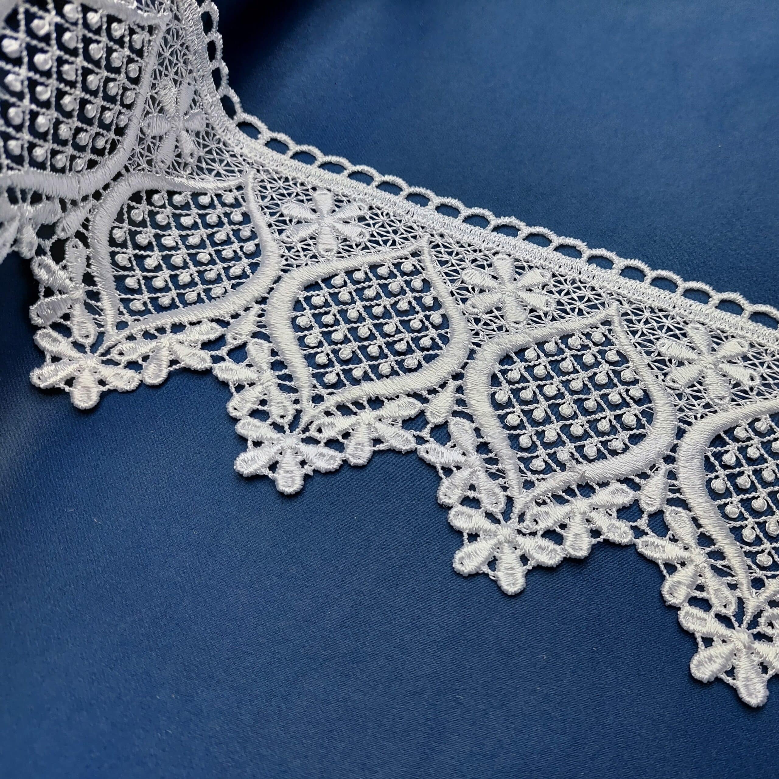 Biała koronka z detalem geometrycznym na niebieskim tle, elegancki wzór ozdobny.