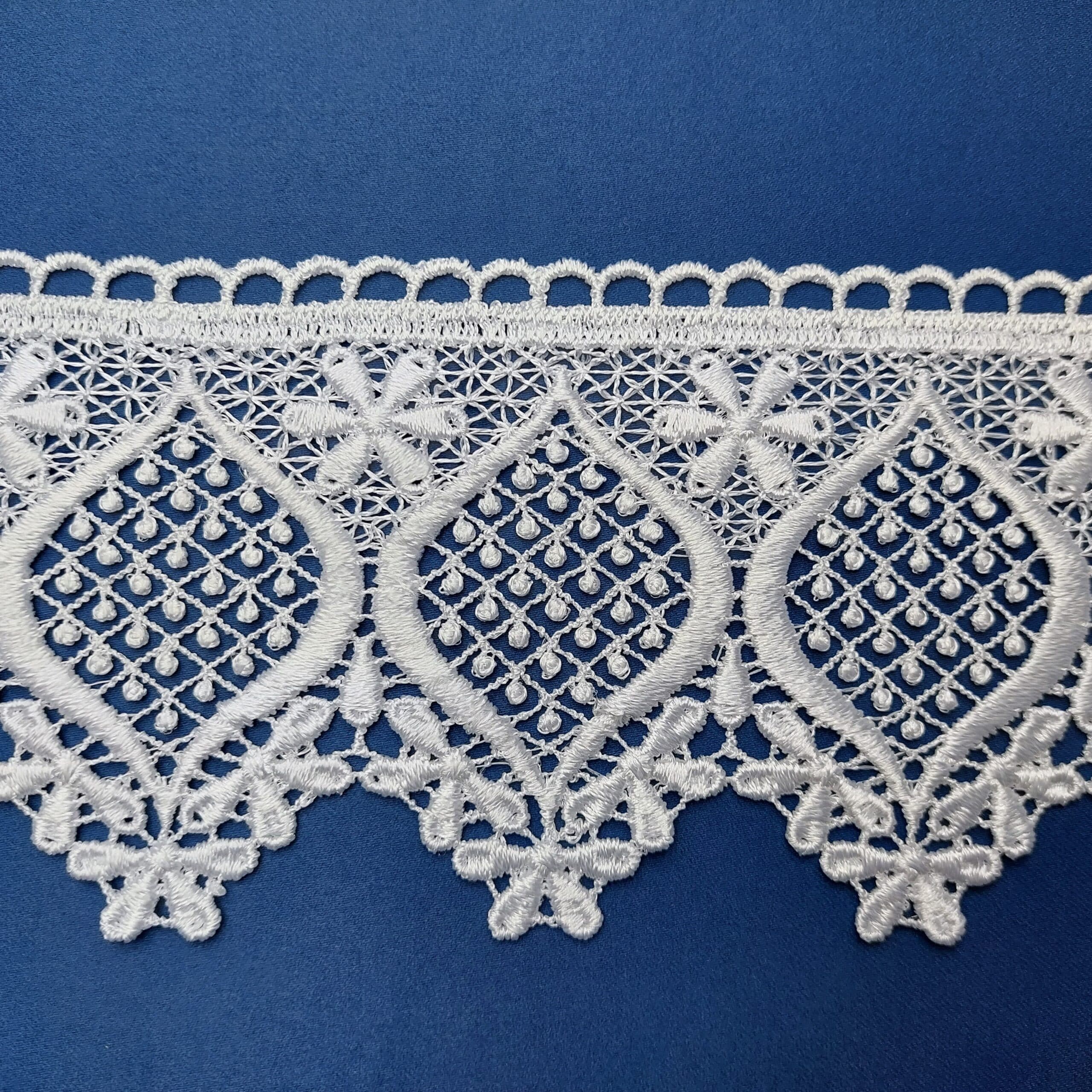 Biała koronka z delikatnym wzorem na niebieskim tle, elegancka i ozdobna, idealna na wykończenie tkanin.