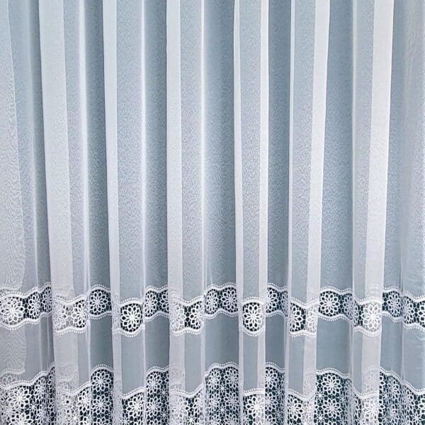 Białe firany z koronkowym wzorem na dole, delikatny materiał zapewnia elegancki wygląd i przepuszcza światło.