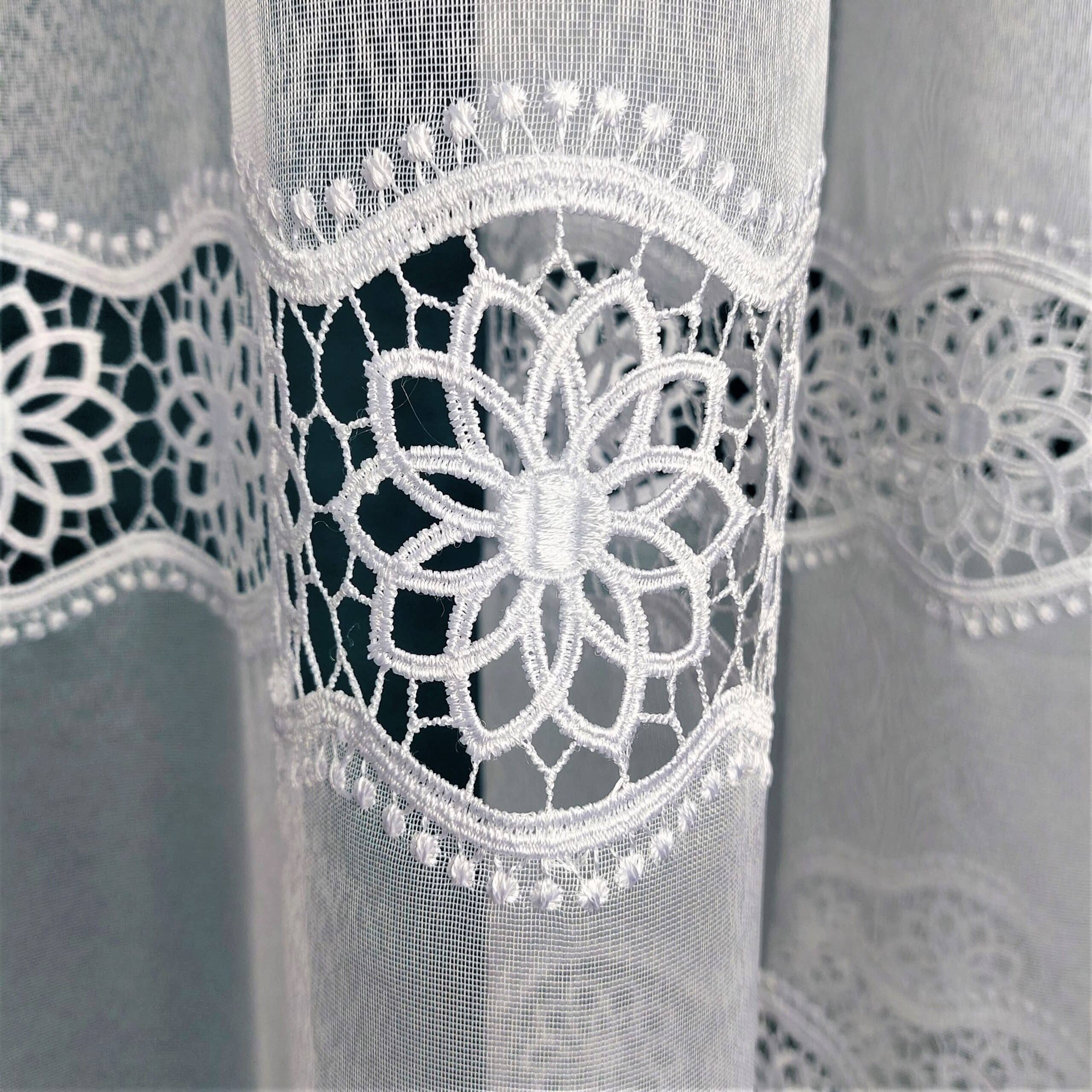 Koronkowa firanka zdobiona kwiatowym wzorem na przezroczystym tle, delikatna i elegancka dekoracja okienna.