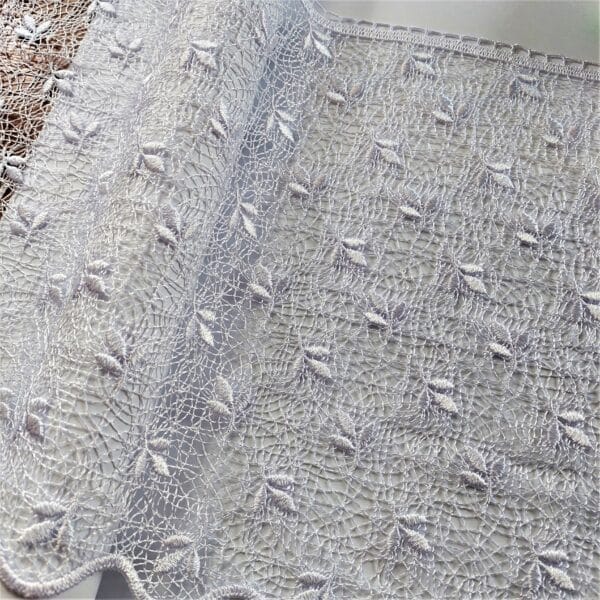 Koronkowa tkanina z delikatnym wzorem kwiatowym w jasnym odcieniu, idealna do dekoracji wnętrz.
