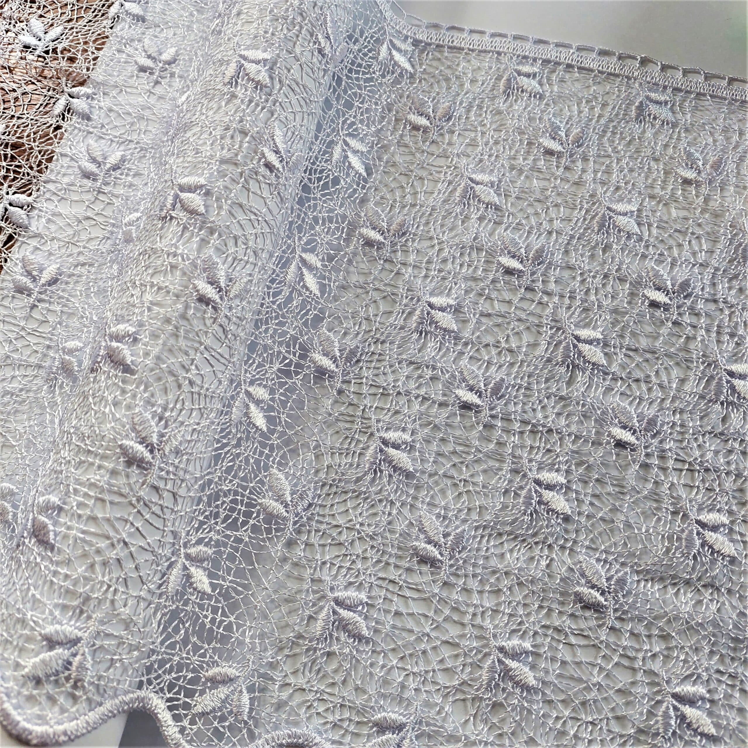 Koronkowa tkanina z delikatnym wzorem kwiatowym w jasnym odcieniu, idealna do dekoracji wnętrz.