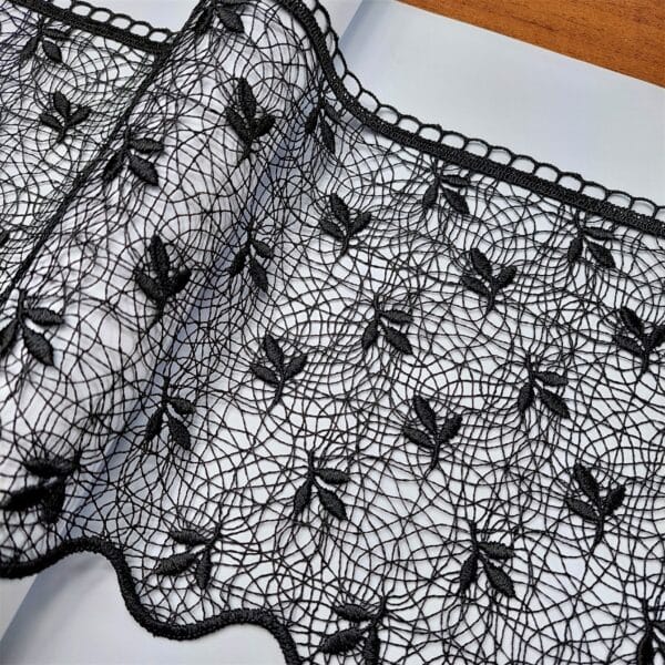 Czarna koronka z kwiatowym wzorem na białym tle, elegancki materiał dekoracyjny.