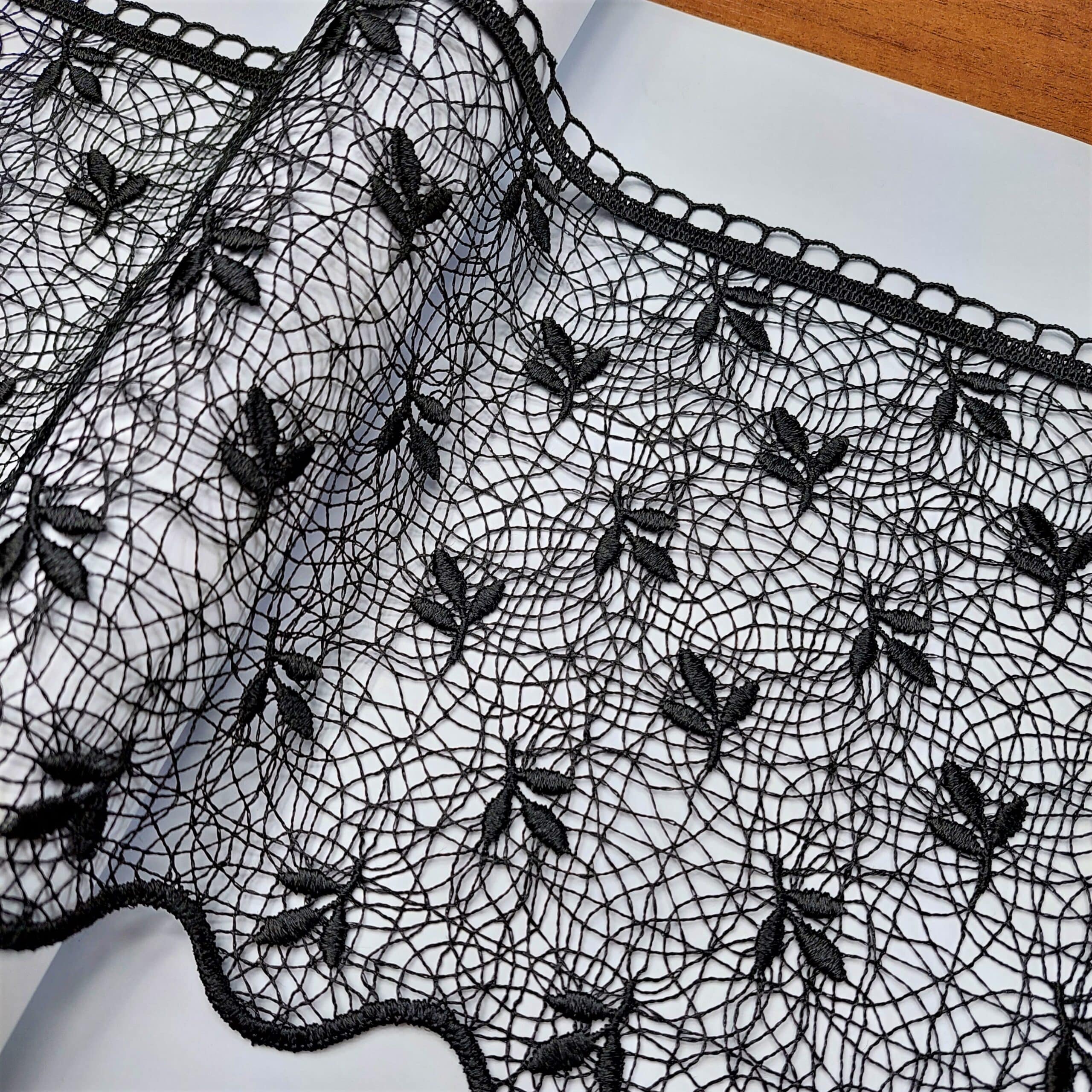 Czarna koronka z kwiatowym wzorem na białym tle, elegancki materiał dekoracyjny.