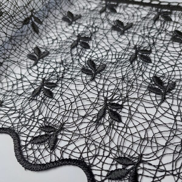 Czarna koronka z wzorem liści na białym tle, delikatna tkanina idealna na eleganckie kreacje.