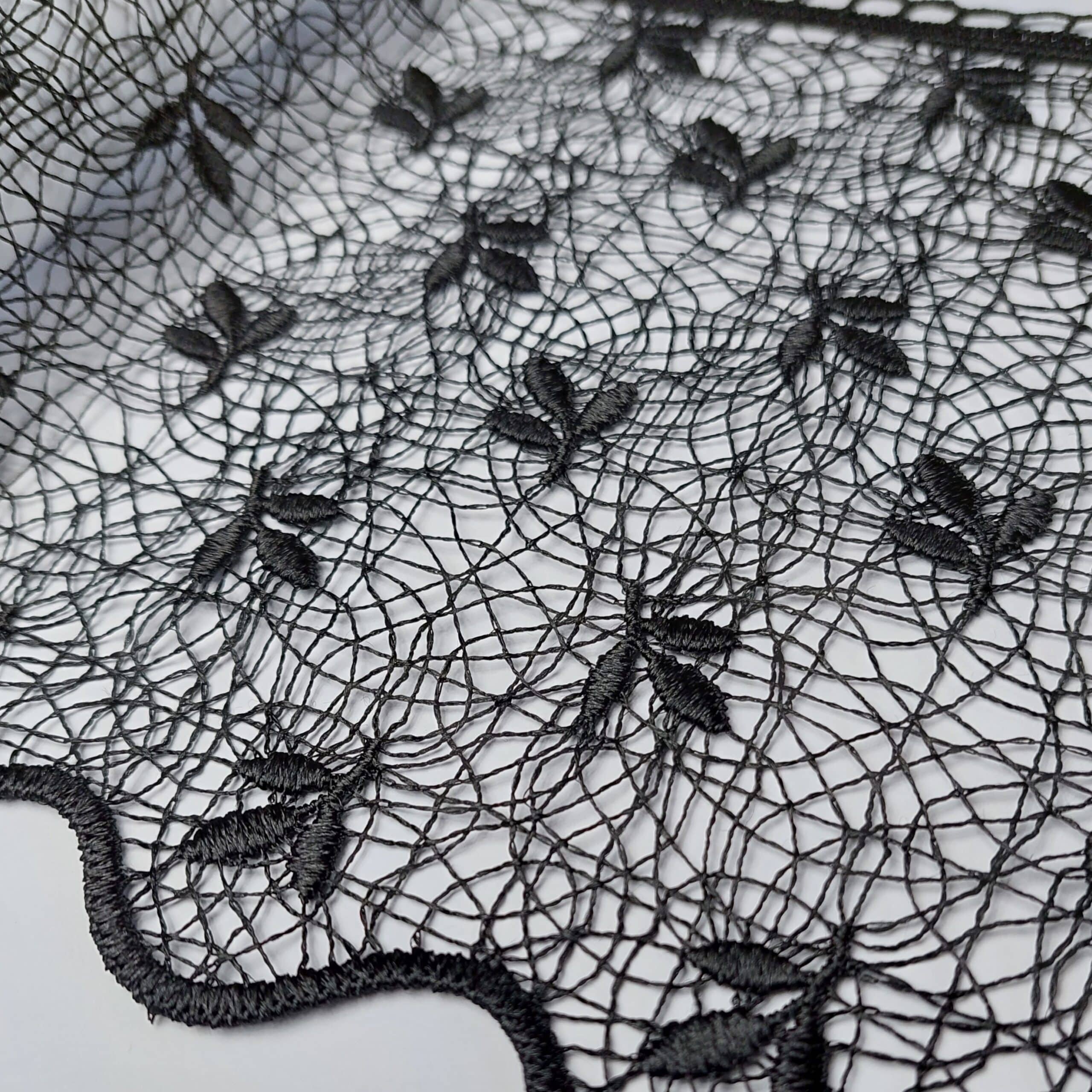 Czarna koronka z wzorem liści na białym tle, delikatna tkanina idealna na eleganckie kreacje.