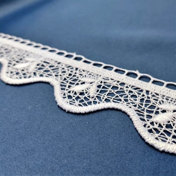 Koronkowa taśma biała na niebieskim tle, delikatny wzór z motywem liści.