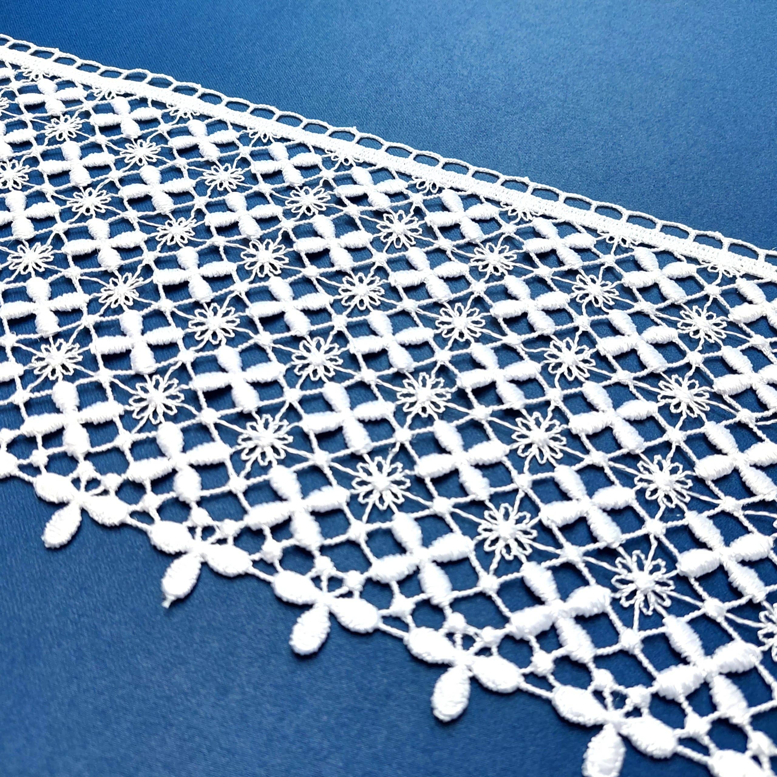 Biały koronkowy wzór na niebieskim tle, dekoracyjna tkanina z motywem kwiatowym i geometrycznym.