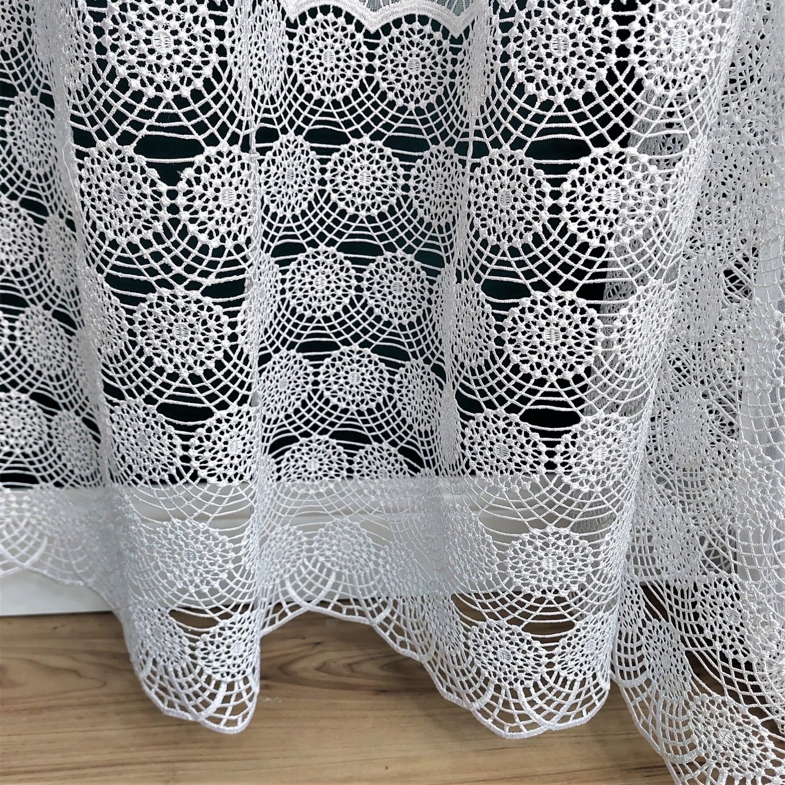 Koronkowa zasłona w białym kolorze z delikatnym wzorem na drewnianej podłodze.