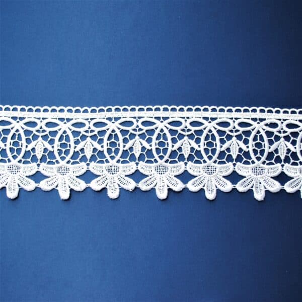Koronkowa biała taśma na niebieskim tle, przedstawiająca delikatny wzór kwiatowy.