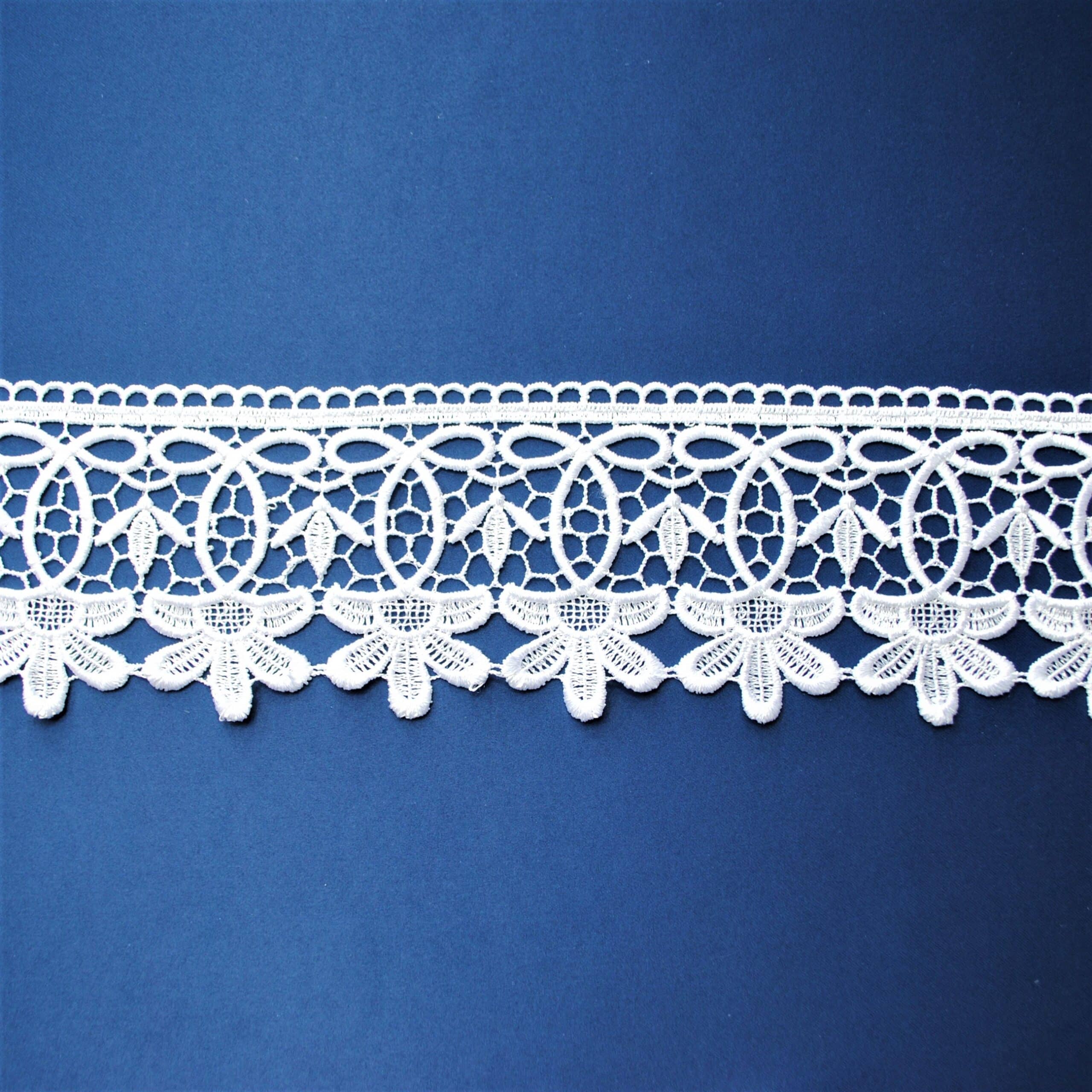 Koronkowa biała taśma na niebieskim tle, przedstawiająca delikatny wzór kwiatowy.