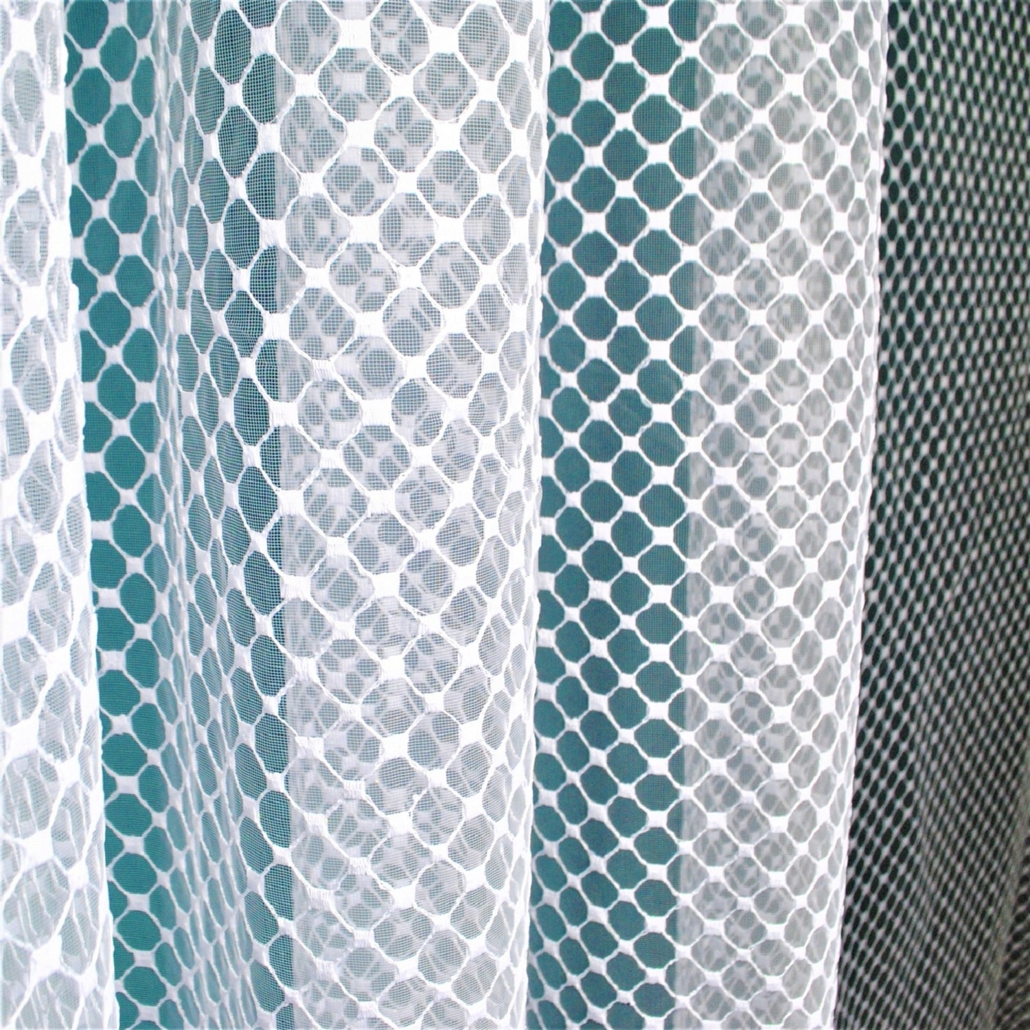 Białe firany z geometrycznym wzorem na tle turkusowej ściany.