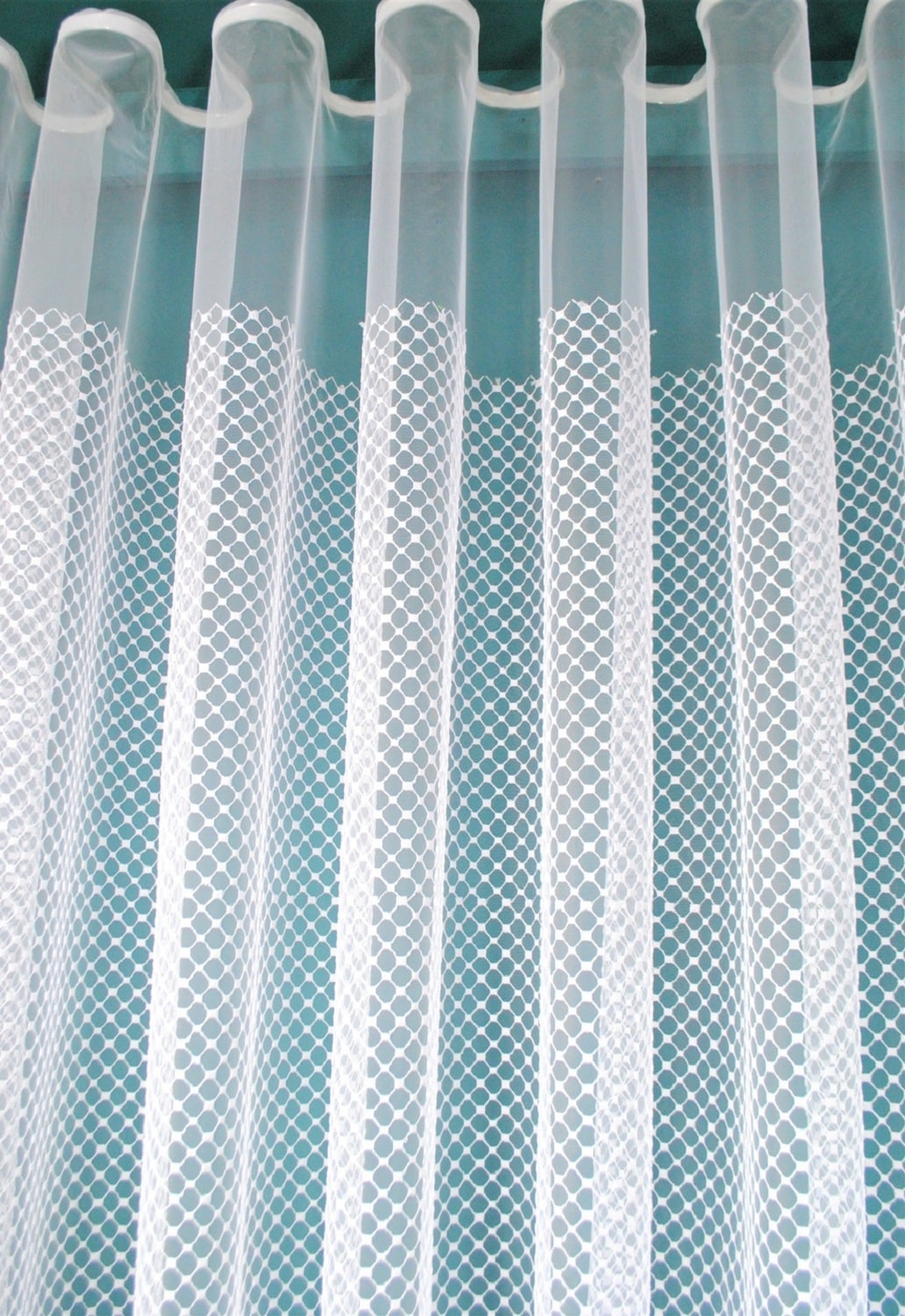 Przezroczyste firanki z wzorem kratki, wiszące na karniszu w jasnym wnętrzu.