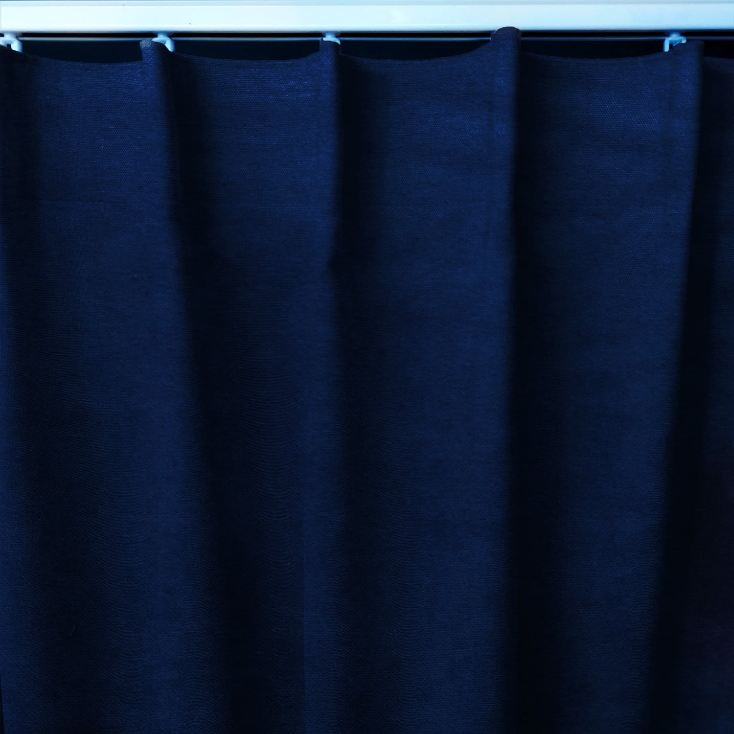 Marszczenie 1 12665_zmiana Granatowa zasłona z falistym wykończeniem, zawieszona na metalowym karniszu.