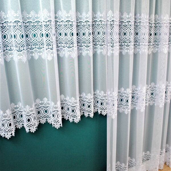 Białe koronkowe firanki w salonie, ozdobne wzory, zielona ściana w tle, drewniana podłoga.