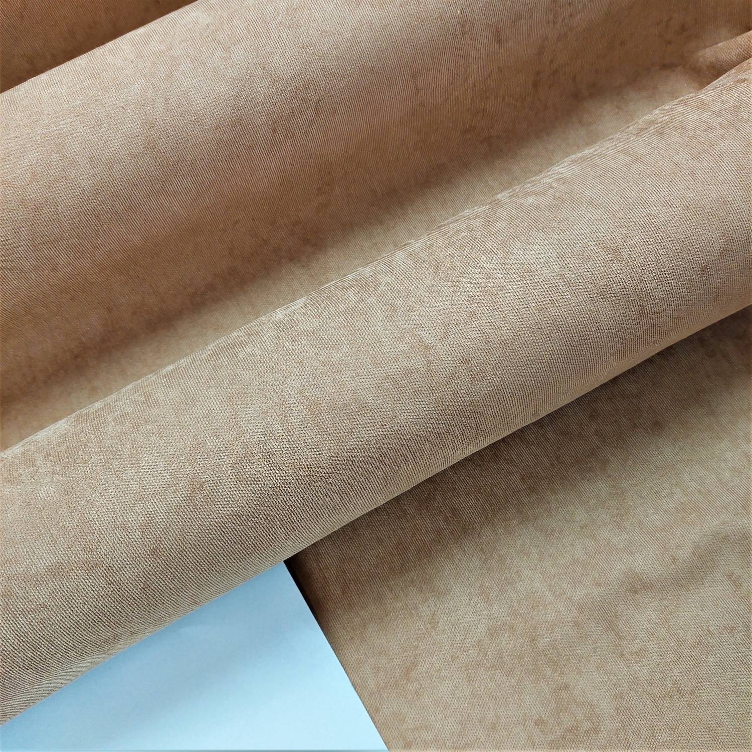 Beżowy materiał obiciowy z bliska, tekstura i wzór widoczne na zagięciach tkaniny.