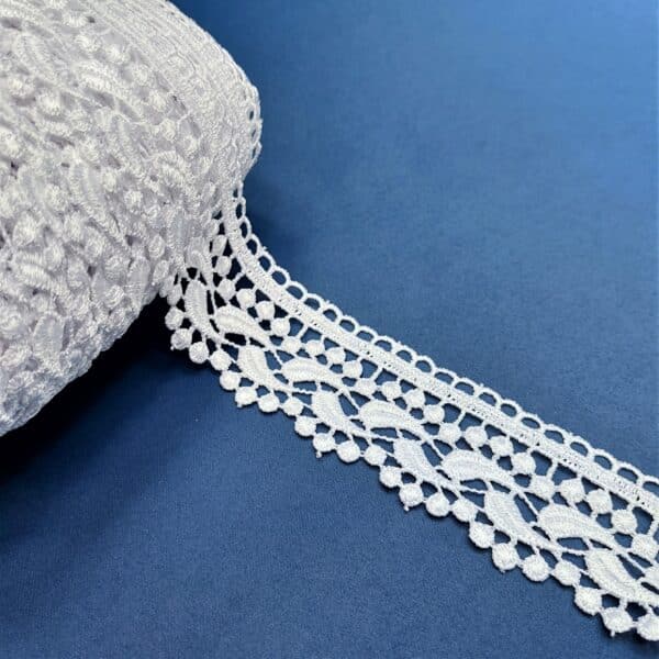 Biała koronka na rolce na niebieskim tle, ozdobna tasiemka do szycia i rękodzieła.
